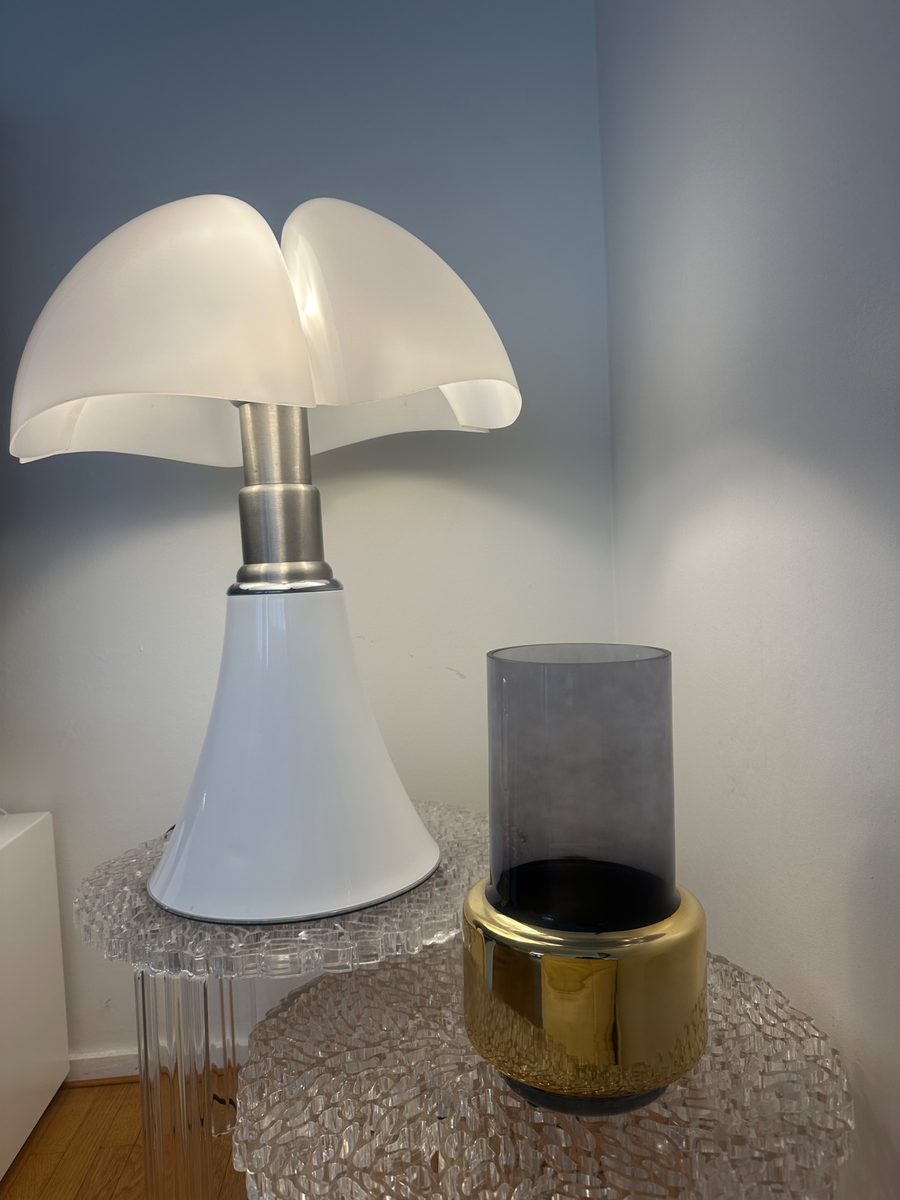 Lampe blanche allumée sur une table d'appoint en verre texturé, à côté d'un photophore fumé et doré